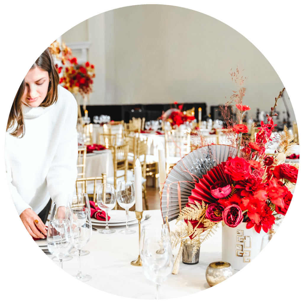 woman checking on details of a table set with red flower centerpieces and red napkins